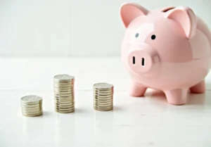 a pink piggy sitting next to stacks of coins on a white table